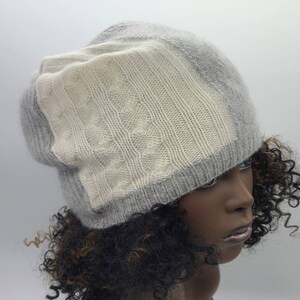 May include: A gray and white knitted beanie with a cable knit pattern. The beanie is slouchy and has a fold-over brim.
