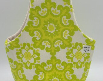 May include: A green and white tote bag with a floral pattern. The bag has a small white label with a simple line drawing of a face on it.