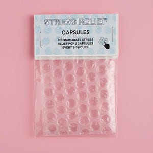 May include: A clear plastic package containing bubble wrap, with a white label that reads "STRESS RELIEF CAPSULES." The label also includes instructions: "FOR IMMEDIATE STRESS RELIEF POP 2 CAPSULES EVERY 2-3 HOURS."