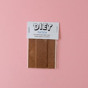 Pode incluir: Um pacote de adesivos de dieta em um fundo rosa. O cabeçalho branco diz "DIET PATCH" com o texto "PLACE PATCH OVER MOUTH UNTIL DESIRED WEIGHT IS ACHIEVED" abaixo. Os adesivos são marrons.
