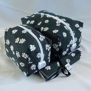 Puede incluir: Tres bolsas de cremallera florales en blanco y negro con lunares blancos. Las bolsas son de diferentes tamaños y están apiladas.