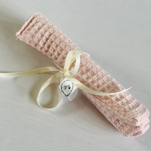 May include: A pink waffle weave cloth is rolled up and tied with a cream ribbon. A small white tag with black lettering is attached to the ribbon. The tag says "The Shop at the End of the Lane".