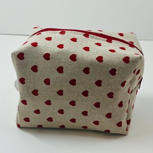 Puede incluir: Una bolsa de cremallera beige con un patr&oacute;n de corazones rojos.