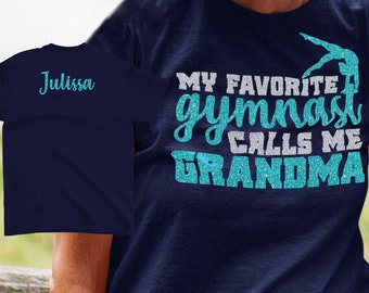 May include: Navy blue t-shirt with turquoise glitter text that reads "My favorite gymnast calls me Grandma". A gymnast silhouette is shown in the text. The back of the shirt has the name "Julissa" in white text.