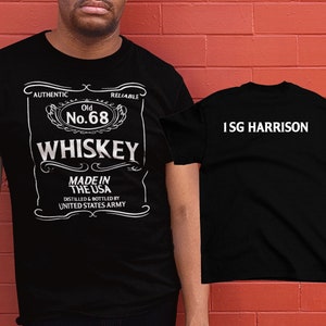 May include: Black t-shirt with a white graphic of a whiskey label that says "Old No. 68 Whiskey Made in the USA Distilled & Bottled by United States Army". The back of the shirt says "ISG HARRISON".