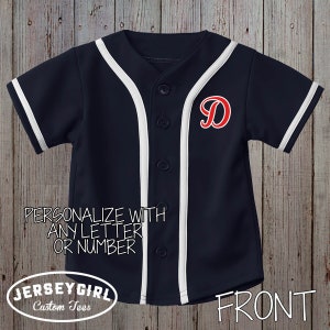 Puede incluir: Una camiseta de b&eacute;isbol azul marino con ribetes blancos y una letra "D" roja en la parte delantera. La camiseta se personaliza con cualquier letra o n&uacute;mero. "PERSONALIZE WITH ANY LETTER OR NUMBER" y "JERSEY GIRL Custom Tees" est&aacute;n impresos en la parte delantera de la camiseta. "FRONT" est&aacute; impreso en la esquina inferior derecha de la camiseta.