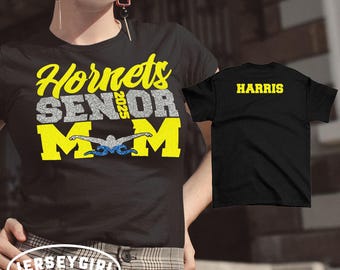 May include: Black t-shirt with yellow text that reads "Hornets Senior 2025 Mom" with a swimmer graphic. A second black t-shirt with yellow text that reads "HARRIS".
