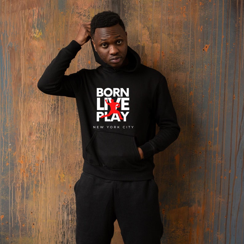 K&ouml;nnte beinhalten: Schwarzer Kapuzenpullover mit wei&szlig;em Text, der "BORN LIVE PLAY" und "NEW YORK CITY" in gestapelter Form lautet. Eine rote Silhouette einer Person, die Basketball spielt, befindet sich zwischen den W&ouml;rtern "LIVE" und "PLAY".