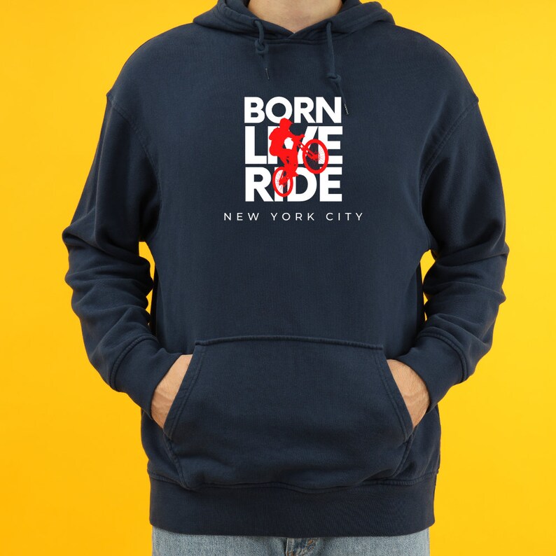 K&ouml;nnte beinhalten: Ein marineblauer Hoodie mit einer wei&szlig;en Grafik, auf der "BORN LIVE RIDE" steht, mit einer roten Silhouette einer Person, die Fahrrad f&auml;hrt. Der Text "NEW YORK CITY" befindet sich unter der Grafik.