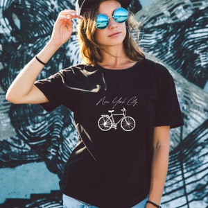 K&ouml;nnte beinhalten: Schwarzes T-Shirt mit einem wei&szlig;en Grafikdruck eines Fahrrads und dem Text "New York City".