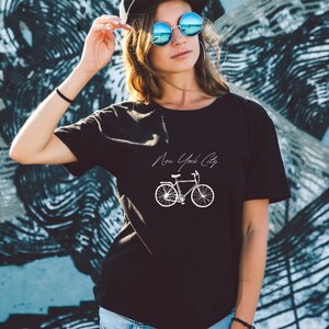 Może przedstawiać: Czarny T-shirt z białym nadrukiem roweru i tekstem "New York City".
