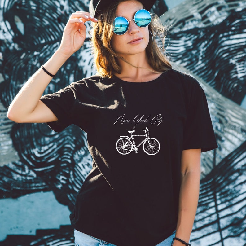 Może przedstawiać: Czarny T-shirt z białym nadrukiem roweru i tekstem "New York City".
