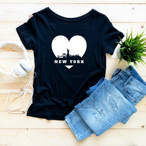 Może przedstawiać: Czarny T-shirt z dekoltem w kształcie litery V z białym sercem z grafiką przedstawiającą panoramę Nowego Jorku i napisem "NEW YORK".