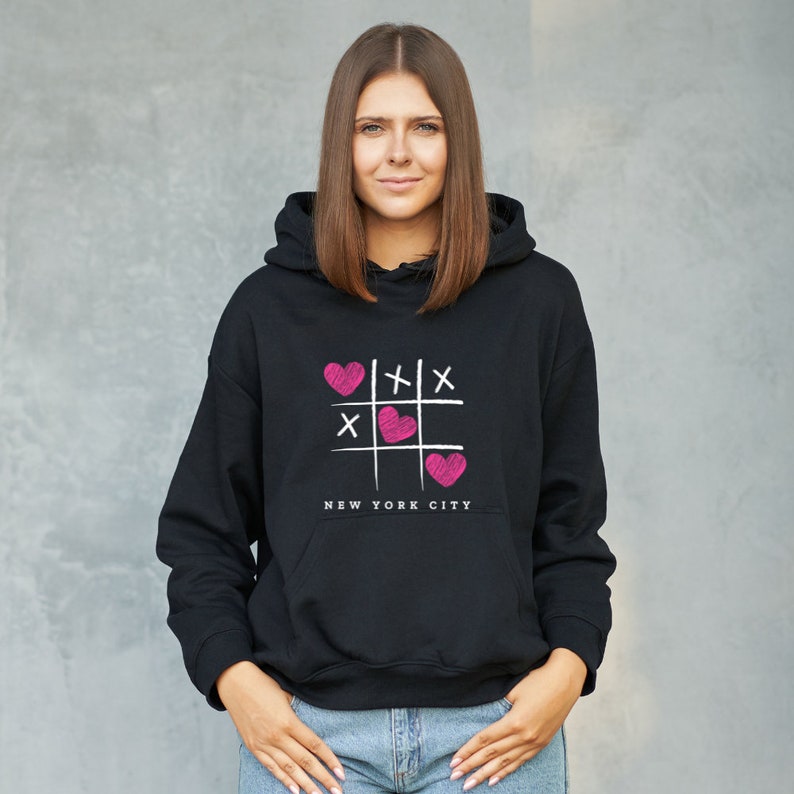 K&ouml;nnte beinhalten: Schwarzer Kapuzenpullover mit einem pinkfarbenen und wei&szlig;en Grafikdruck eines Tic-Tac-Toe-Spielfelds mit Herzen und dem Text "NEW YORK CITY".