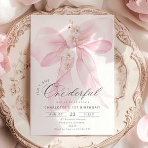 Puede incluir: Una invitaci&oacute;n rosa y blanca con una ilustraci&oacute;n de acuarela de un lazo y flores. El texto dice "Isn't She Onederful" e incluye detalles para la fiesta de cumplea&ntilde;os n&uacute;mero 1 de Charlotte.