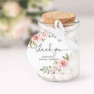 May include: A round, white thank you tag with pink and green floral illustrations. The tag says "thank you" in cursive and "Jennifer's Bridal Shower".