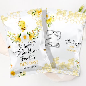 Könnte beinhalten: Zwei weiße Party-Geschenktüten mit Bienen-Motiv. Eine Tüte zeigt eine Cartoon-Biene, Blumen und den Text "So sweet to bee One Jennifer's BEE-DAY! 08.10.2023." Die andere Tüte hat ein Nährwertetikett und "thank you for coming!"