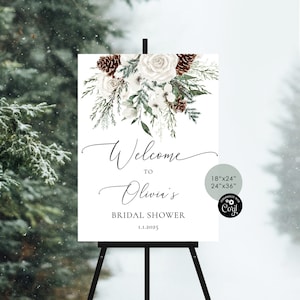 May include: A white welcome sign with a winter floral design featuring white roses, pine cones, and greenery. The sign reads "Welcome to Olivia's Bridal Shower 1.1.2025". The sign is available in two sizes: 18" x 24" and 24" x 36".