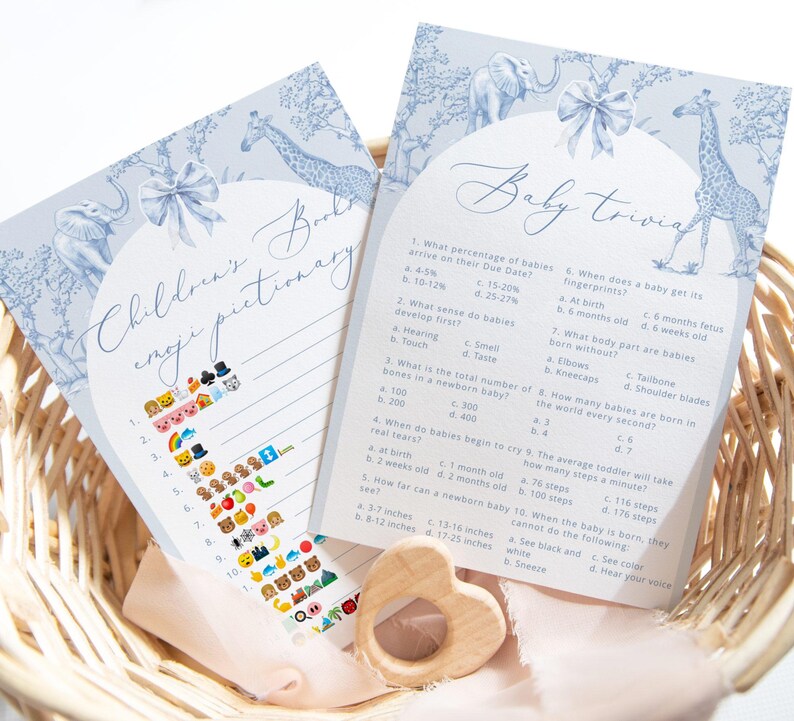 K&ouml;nnte beinhalten: Zwei blaue und wei&szlig;e Babyparty-Spielkarten mit einem Giraffen- und Elefanten-Design. Die erste Karte ist ein Emoji-Pictionary-Spiel f&uuml;r Kinder mit einer Liste von Emojis und Zahlen. Die zweite Karte ist ein Baby-Quiz mit Fragen &uuml;ber Babys und ihre Entwicklung.