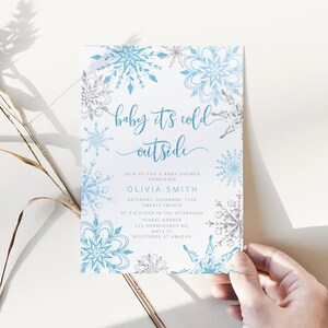 Pu&ograve; includere: Un invito per un baby shower a tema invernale. L'invito presenta uno sfondo bianco con disegni di fiocchi di neve blu e argento. Il testo "baby it's cold outside" &egrave; scritto in un carattere script. Include nome, data, ora e luogo.