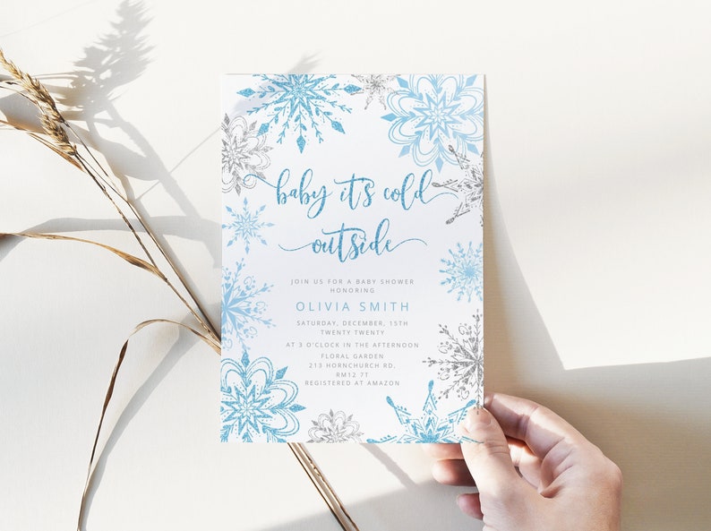 Pu&ograve; includere: Un invito per un baby shower a tema invernale. L'invito presenta uno sfondo bianco con disegni di fiocchi di neve blu e argento. Il testo "baby it's cold outside" &egrave; scritto in un carattere script. Include nome, data, ora e luogo.