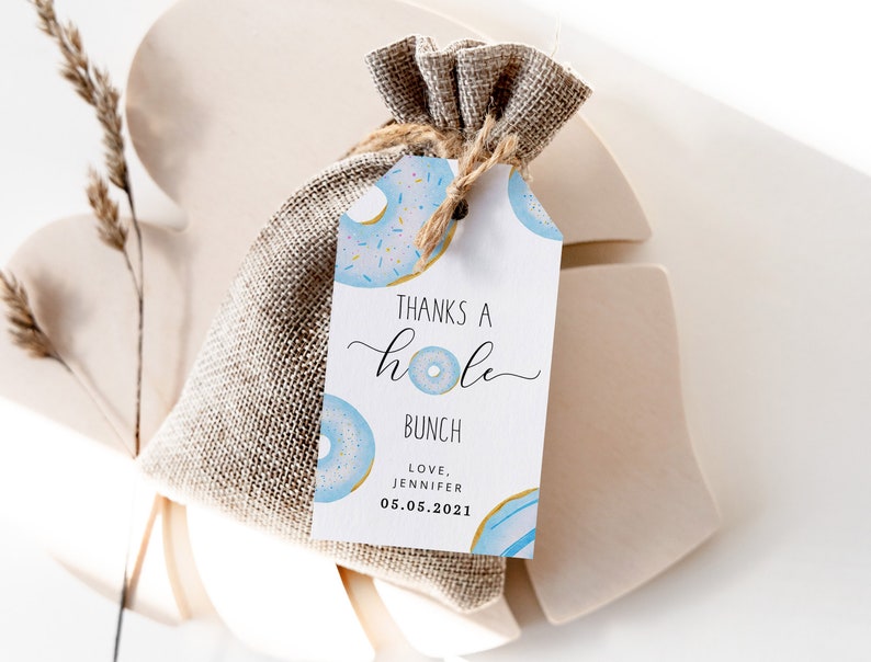 May include: A white favor tag with blue and gold donuts and the text "Thanks a hole bunch, Love, Jennifer 05.05.2021".