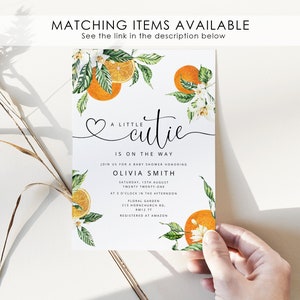 May include: A white baby shower invitation featuring a watercolour illustration of orange blossoms and oranges. The text reads "A little cutie is on the way" and includes the event details, including the date, time, and location. The invitation also includes the name of the guest of honour, Olivia Smith, and the information that the event is registered at Amazon.