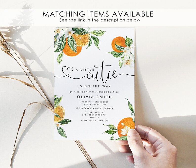 May include: A white baby shower invitation featuring a watercolour illustration of orange blossoms and oranges. The text reads "A little cutie is on the way" and includes the event details, including the date, time, and location. The invitation also includes the name of the guest of honour, Olivia Smith, and the information that the event is registered at Amazon.