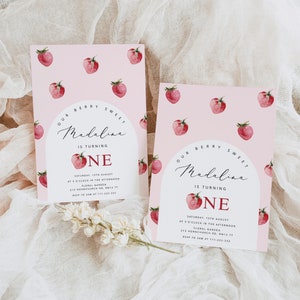 May include: Pink invitation with a red strawberry pattern. The invitation says "Our Berry Sweet Madalina is turning One" with a red strawberry graphic. The invitation includes the date, time, location, and RSVP information.