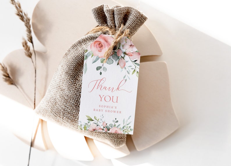 May include: A white thank you tag with pink floral illustrations and the text "Thank You Sophia's Baby Shower". The tag is tied to a small burlap bag.