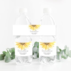 May include: Two clear plastic water bottles with white labels featuring a watercolor sunflower design. The labels have the text "Samantha's Baby Shower 05.06.2023".