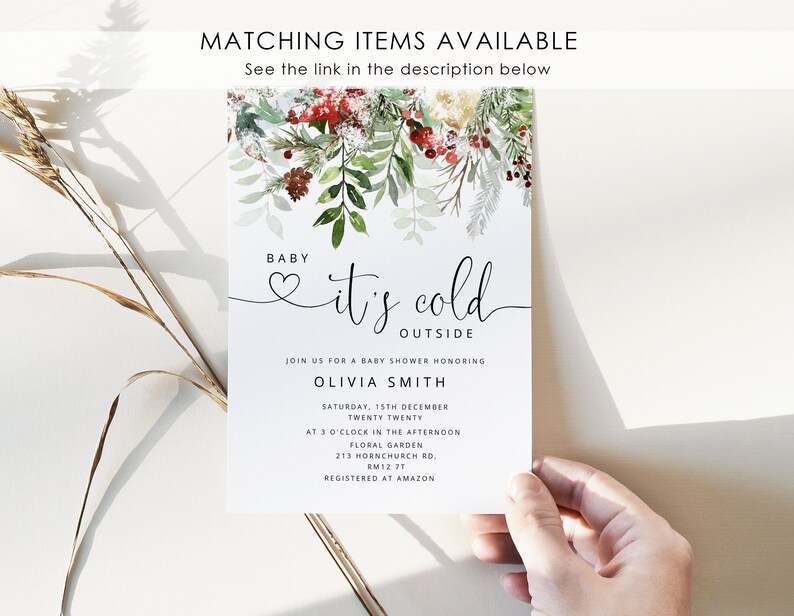 Op de afbeelding: Een witte babyshower-uitnodiging met een aquarel-illustratie van wintergroen en rode bessen. De tekst luidt "Baby it's cold outside" en bevat details over het evenement, inclusief de datum, tijd en locatie. De uitnodiging is geregistreerd bij Amazon.