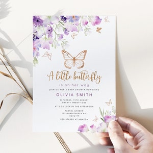 Może przedstawiać: Zaproszenie na baby shower z akwarelowym wzorem kwiatowym w odcieniach fioletu i błękitu. Zaproszenie zawiera złotego motyla i tekst "A little butterfly is on her way." Zaproszenie jest dla Olivii Smith i zawiera datę, godzinę i miejsce imprezy. Tekst "Registered at Amazon" r&oacute;wnież jest uwzględniony.