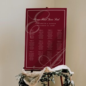 May include: A burgundy wedding seating chart on an easel. The chart features the text "Please Find Your Seat" and the names of the bride and groom, Elizabeth and Andrew, with the date November 25, 2028. The chart is framed in white.