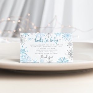 Pu&ograve; includere: Biglietto d'invito per baby shower con un design a fiocco di neve. Il biglietto presenta il testo "books for baby" in un carattere a script, insieme a una richiesta agli ospiti di portare un libro invece di un biglietto. Il biglietto &egrave; decorato con fiocchi di neve blu e argento.