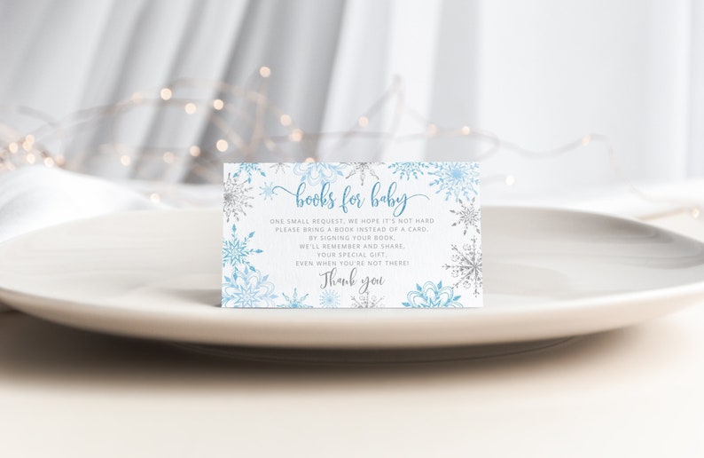 Pu&ograve; includere: Biglietto d'invito per baby shower con un design a fiocco di neve. Il biglietto presenta il testo "books for baby" in un carattere a script, insieme a una richiesta agli ospiti di portare un libro invece di un biglietto. Il biglietto &egrave; decorato con fiocchi di neve blu e argento.