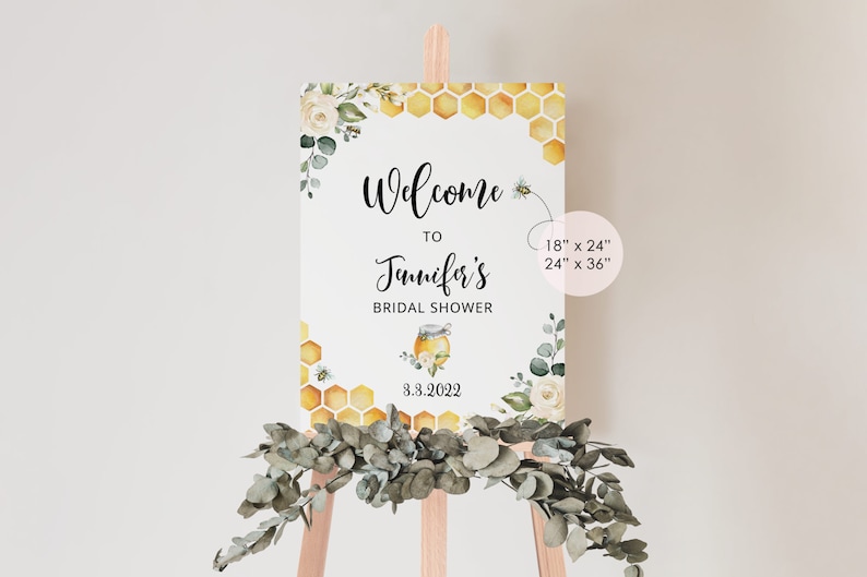May include: Welcome to Jennifer's Bridal Shower sign with a honey pot and bee design. The sign is decorated with white flowers and green leaves. The sign is available in two sizes: 18" x 24" and 24" x 36".