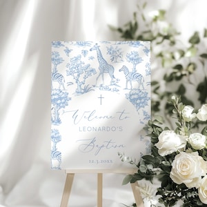 Op de afbeelding: Blauw en wit doopsel welkomstbord met een toile-de-jouy patroon met giraffen en zebra's. De tekst "Welcome to Leonardo's Baptism" en de datum 12.3.20XX zijn zichtbaar. Het bord staat op een houten ezel.