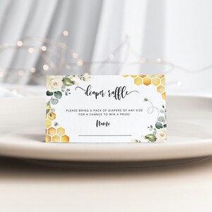 May include: White card with a floral design and honeycomb pattern. The text reads "diaper raffle" and "Please bring a pack of diapers of any size for a chance to win a prize!" with a line for a name.