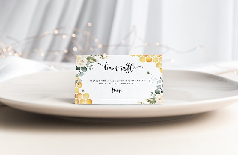 May include: White card with a floral design and honeycomb pattern. The text reads "diaper raffle" and "Please bring a pack of diapers of any size for a chance to win a prize!" with a line for a name.