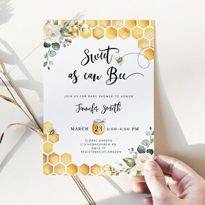 May include: A baby shower invitation with a watercolor illustration of a honeycomb, white flowers, and green leaves. The text reads "Sweet as can Bee" and includes the date, time, and location of the event. The invitation is for Jennifer Smith.