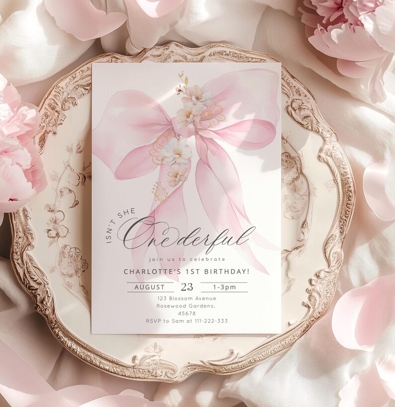Puede incluir: Una invitaci&oacute;n rosa y blanca con una ilustraci&oacute;n de acuarela de un lazo y flores. El texto dice "Isn't She Onederful" e incluye detalles para la fiesta de cumplea&ntilde;os n&uacute;mero 1 de Charlotte.