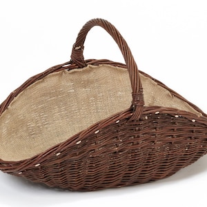 Könnte beinhalten: Ein brauner Korb aus geflochtenem Weidengeflecht mit einem gebogenen Griff. Der Korb hat ein Innenfutter aus Jute und ein breites, offenes Design. Ideal zum Tragen von Gegenständen oder als dekoratives Element.
