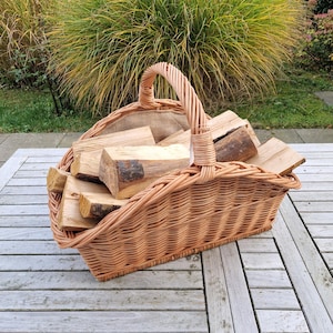 Könnte beinhalten: Ein hellbrauner Weidenkorb gefüllt mit Brennholz. Der Korb hat einen gebogenen Griff und ist mit mehreren Stücken geschnittenem Holz gefüllt. Der Korb steht auf einem Holztisch.
