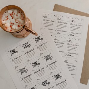 Puede incluir: Una taza de cobre llena de chocolate caliente y malvaviscos, con una hoja de instrucciones y etiquetas de regalo que dicen "&iexcl;Felices Fiestas!" y "&iexcl;Bomba de chocolate caliente!"