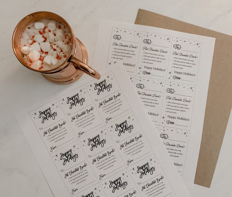 Puede incluir: Una taza de cobre llena de chocolate caliente y malvaviscos, con una hoja de instrucciones y etiquetas de regalo que dicen "&iexcl;Felices Fiestas!" y "&iexcl;Bomba de chocolate caliente!"
