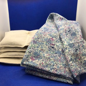 May include: A stack of four beige cushions with a floral patterned fabric folded on top. The fabric is white with blue, pink, and green flowers.