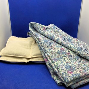 May include: Two beige pillows with a floral patterned fabric folded on top of them. The pillows and fabric are on a blue surface.