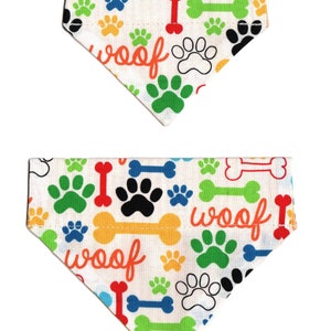 May include: Two white dog bandanas with a colorful paw print and bone pattern. The bandanas have the word "woof" printed on them.