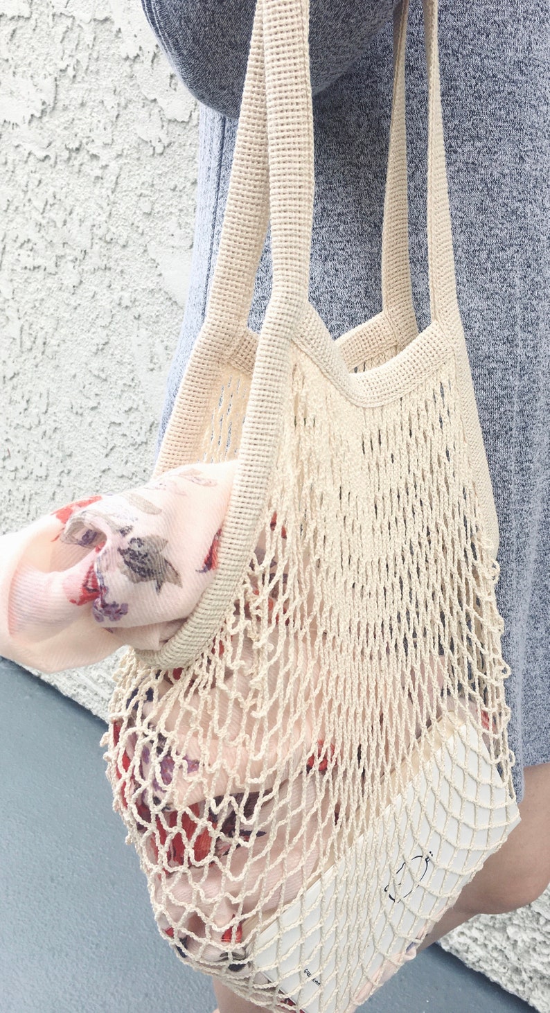 woman holding white net bag on the straps with scarf and planner inside the bag